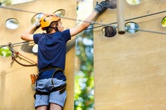 Child In Forest Adventure Park. Kid In Orange Helmet And Blue T Shirt Climbs On High Rope Trail. Agility Skills Stock Image