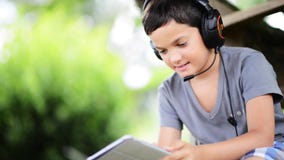 Child listen music and playing on the computer with headphones outdoor stock video footage Child listen music and playing on the computer with headphones outdoor stock video footage