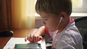 The child listens to music on smartphone in the headphones making lessons stock footage The child listens to music on smartphone in the headphones making lessons stock footage