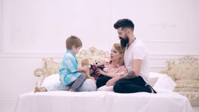 Child, mom and dad sit on bed, smiling and communicate. Young happy couple together in bedroom. Young family being stock video Child, mom and dad sit on bed, smiling and communicate. Young happy couple together in bedroom. Young family being stock video