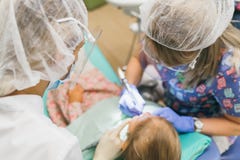 Child with a mother at a dentist`s reception. The girl lies in the chair, behind her mother. The doctor works with an stock photography Child with a mother at a dentist`s reception. The girl lies in the chair, behind her mother. The doctor works with an stock photography