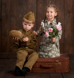 Children boy are dressed as soldier in retro military uniforms and girl in pink dress sitting on old suitcase, dark wood backgroun stock image Children boy are dressed as soldier in retro military uniforms and girl in pink dress sitting on old suitcase, dark wood backgroun stock image