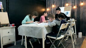 Children boys and girls sitting together around the table in classroom and drawing. With them is their young and stock photos Children boys and girls sitting together around the table in classroom and drawing. With them is their young and stock photos