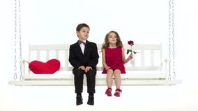 Children ride on a swing, they have a romantic relationship. White background. Slow motion. Children ride on a white swing, a little girl has a rose in her hand Children ride on a swing, they have a romantic relationship. White background. Slow motion. Children ride on a white swing, a little girl has a rose in her hand