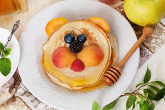 Children's breakfast pancakes smiling face of the baby teddy bear strawberry blueberry and apricot, cute food, honey