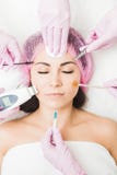Chiuda su di bello fronte di una giovane donna Molte mani che tengono gli strumenti di cosmetologia vicino al paziente del fronte fotografia stock Chiuda su di bello fronte di una giovane donna Molte mani che tengono gli strumenti di cosmetologia vicino al paziente del fronte fotografia stock