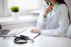 Chiuda su di medico femminile sconosciuto che si siede alla tavola vicino alla finestra in ospedale Fotografia Stock Libera da Diritti Chiuda su di medico femminile sconosciuto che si siede alla tavola vicino alla finestra in ospedale Fotografia Stock Libera da Diritti