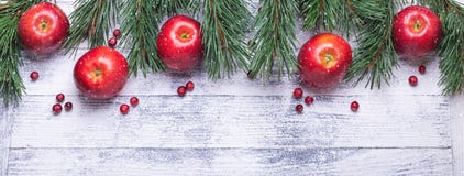 Christmas background with tree branches, red apples and cranberries. Light wooden table. Snowfall drawing effect royalty free stock image Christmas background with tree branches, red apples and cranberries. Light wooden table. Snowfall drawing effect royalty free stock image