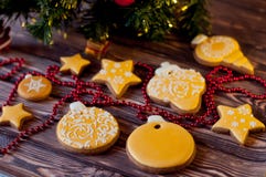 Christmas decorations. Honey cookies, glazed by yellow, white patterns laying near red beads, green pine tree branch on wooden tab Royalty Free Stock Image Christmas decorations. Honey cookies, glazed by yellow, white patterns laying near red beads, green pine tree branch on wooden tab Royalty Free Stock Image