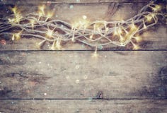 Christmas warm gold garland lights on wooden rustic background. filtered image with glitter overlay.