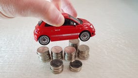 Chwyty w jego palca Fiat 500 małej czerwonej zabawce nad stosem jeden syklu Izraelickie monety obrazy stock Chwyty w jego palca Fiat 500 małej czerwonej zabawce nad stosem jeden syklu Izraelickie monety obrazy stock
