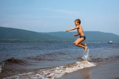 Chłopiec skacze nad falami na plaży dzień sunny lato fotografia stock Chłopiec skacze nad falami na plaży dzień sunny lato fotografia stock