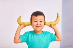 Chłopiec dziecko zakrywał jego ucho z bananami obraz royalty free Chłopiec dziecko zakrywał jego ucho z bananami obraz royalty free