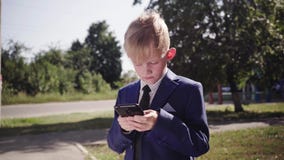 Chłopiec w kostiumu trzyma smartphone i bawić się grę na ulicie zbiory Chłopiec w kostiumu trzyma smartphone i bawić się grę na ulicie zbiory