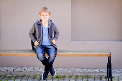 Chłopiec z plecaka obsiadaniem na ławce blisko szkoły zdjęcia royalty free Chłopiec z plecaka obsiadaniem na ławce blisko szkoły zdjęcia royalty free
