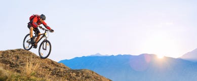 Ciclista na equita??o vermelha a bicicleta abaixo da rocha no nascer do sol Esporte extremo e conceito Biking de Enduro foto de stock Ciclista na equita??o vermelha a bicicleta abaixo da rocha no nascer do sol Esporte extremo e conceito Biking de Enduro foto de stock