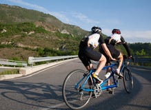 Ciclistas em uma montada em tandem da bicicleta subida em uma estrada da montanha imagem de stock royalty free Ciclistas em uma montada em tandem da bicicleta subida em uma estrada da montanha imagem de stock royalty free