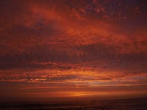 Cielo rojo vivo en la puesta del sol en la playa con las nubes dramáticas y el mar oscuro fotos de archivo Cielo rojo vivo en la puesta del sol en la playa con las nubes dramáticas y el mar oscuro fotos de archivo
