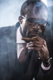 Cigarro que fuma del hombre de negocios afroamericano confiado fotos de archivo Cigarro que fuma del hombre de negocios afroamericano confiado fotos de archivo