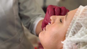 Ciérrese para arriba de la mujer joven que se prepara a la inyección del ácido hialurónico a los labios almacen de metraje de vídeo Ciérrese para arriba de la mujer joven que se prepara a la inyección del ácido hialurónico a los labios almacen de metraje de vídeo