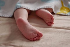Ciérrese para arriba de los pies del bebé que miran a escondidas de la manta El niño está durmiendo fotografía de archivo libre de regalías Ciérrese para arriba de los pies del bebé que miran a escondidas de la manta El niño está durmiendo fotografía de archivo libre de regalías