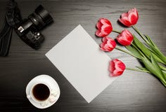 Clean sheet of paper, pink tulips, a camera and a mug of coffee. Black table. top view Stock Photography Clean sheet of paper, pink tulips, a camera and a mug of coffee. Black table. top view Stock Photography