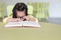 Clever little child girl wearing glasses intend reading a book in the kids room