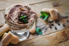 Close-up of classic tiramisu cake in a glass with fresh mint, on wooden background stock photos Close-up of classic tiramisu cake in a glass with fresh mint, on wooden background stock photos