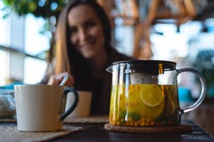 Close-up of a Cup and a glass teapot with sea buckthorn tea with lemon and herbs, on the background of a smiling girl royalty free stock image Close-up of a Cup and a glass teapot with sea buckthorn tea with lemon and herbs, on the background of a smiling girl royalty free stock image