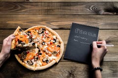 Close-up da pizza e do caderno com o texto: Entrega da pizza tabela de madeira do fundo Preto do caderno com texto branco imagens de stock Close-up da pizza e do caderno com o texto: Entrega da pizza tabela de madeira do fundo Preto do caderno com texto branco imagens de stock