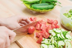 Close-up Delicate Female Hands Cut A Large Knife With Tomatoes On A Quarter On A Wooden Board At Home. Home Kitchen Royalty Free Stock Image