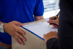 Close up Delivery man in blue uniform holding package while woman is signing receiving documents. stock photo Close up Delivery man in blue uniform holding package while woman is signing receiving documents. stock photo