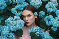 Close Up Face Of Beautiful Young Woman With Red Lips And Blue Eyes And With A Blue Flower Behind Her Ear, Standing Among Royalty Free Stock Image