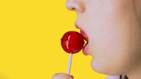 Close-up, female sexy lips suck big pink round lollipop. Yellow background