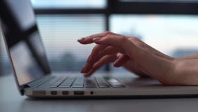 Close-up hands of unrecognizable business woman closing lid of laptop computer at desk on background of window