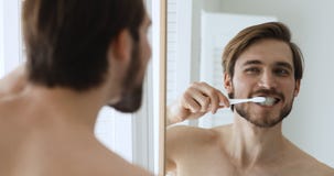 Young happy bare man brushing teeth with toothbrush and toothpaste.