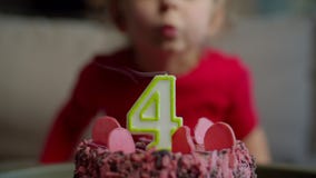 Close up of kid blowing out candle with number 4 on chocolate birthday cake in slow motion. Four years old girl