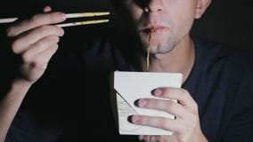 Close-up of a man who is eating noodles with chopsticks from a box. European eating Chinese food stock footage Close-up of a man who is eating noodles with chopsticks from a box. European eating Chinese food stock footage