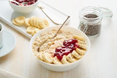 Close up of oatmeal porridge, healthy vegan diet breakfast with strawberry jam, peanut butter, banana, chia on white wooden light stock photography Close up of oatmeal porridge, healthy vegan diet breakfast with strawberry jam, peanut butter, banana, chia on white wooden light stock photography