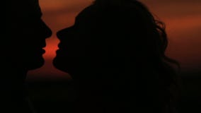 Close-up portrait of the charming silhouette couple gently kissing at the background of the red sky during the sunset.