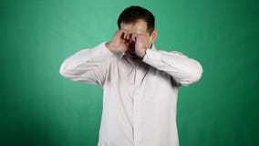 Close-up portrait of a crying man. A young businessman closes his aching eyes with tears on green background stock video Close-up portrait of a crying man. A young businessman closes his aching eyes with tears on green background stock video