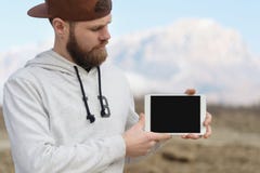 Close-up Portrait of a hipster in a brown cap in the open air holds a white tablet pc in his hands. A bearded man looks royalty free stock photos Close-up Portrait of a hipster in a brown cap in the open air holds a white tablet pc in his hands. A bearded man looks royalty free stock photos