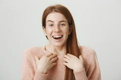 Close-up portrait of sincere pretty ginger girl pointing at herself and laughing, standing against gray background stock photos Close-up portrait of sincere pretty ginger girl pointing at herself and laughing, standing against gray background stock photos