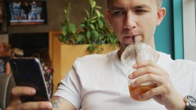 Close-up portrait of young man use mobile phone in cafe, drinks cold coffee cocktail stock video Close-up portrait of young man use mobile phone in cafe, drinks cold coffee cocktail stock video