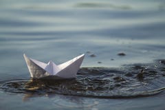 Close-up of simple small white origami paper boat floating in blue clear river or sea water under bright summer sky. Beauty of nat. Ure, freedom, dreams and Royalty Free Stock Photography Close-up of simple small white origami paper boat floating in blue clear river or sea water under bright summer sky. Beauty of nat. Ure, freedom, dreams and Royalty Free Stock Photography