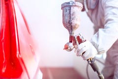Close-up of spray gun with red paint painting a car