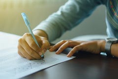 Close up of student`s hand holds a pen write on answer sheet. Student answers multiple choice questions on wooden table in examin Royalty Free Stock Photo Close up of student`s hand holds a pen write on answer sheet. Student answers multiple choice questions on wooden table in examin Royalty Free Stock Photo