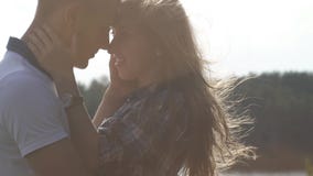 Close up teenager couple in love kissing outdoor at bright sunny day. Light breeze waving girl's hair. Warm filter tone