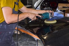 Close-up view on the hands of a male worker in yellow shirt who holds a tool for polishing the hood of a car while working in a royalty free stock images Close-up view on the hands of a male worker in yellow shirt who holds a tool for polishing the hood of a car while working in a royalty free stock images