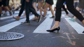 Close-up view of stylish female feet. Businesswoman crossing the road in crowded downtown. Slow motion.